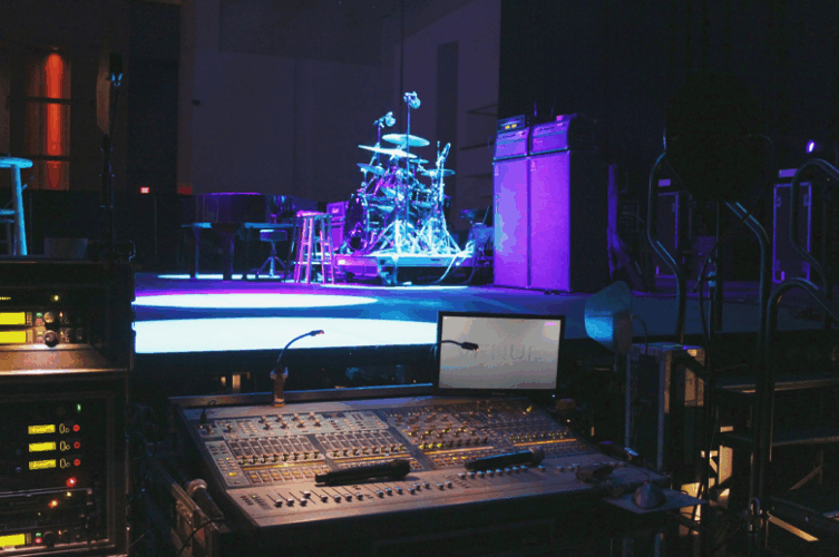 Professional live sound mixing console positioned beside a concert stage